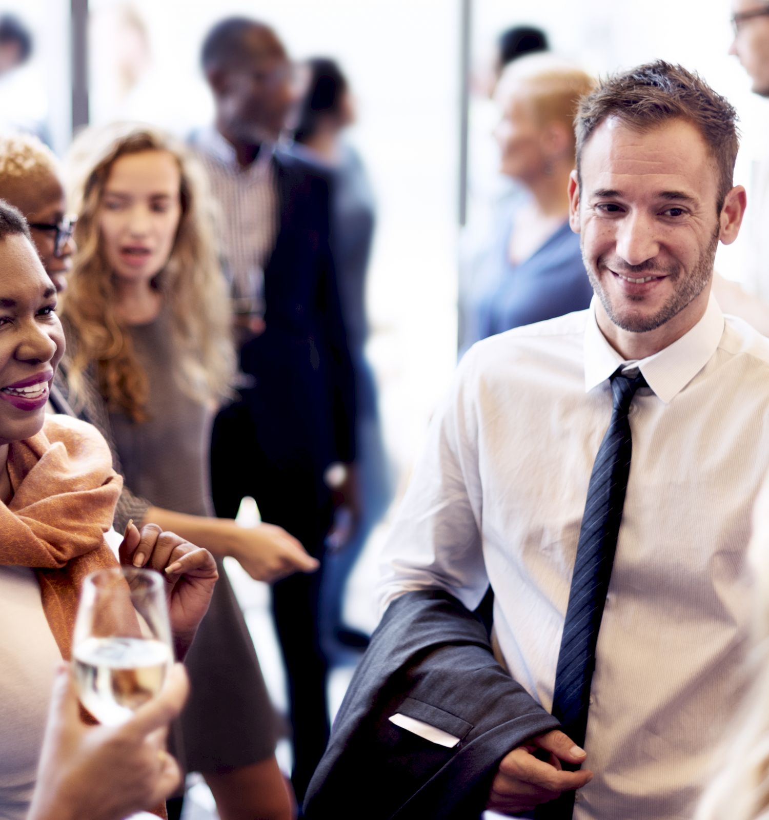 A diverse group of people are socializing at a gathering, some with drinks in hand, smiling and conversing with one another.