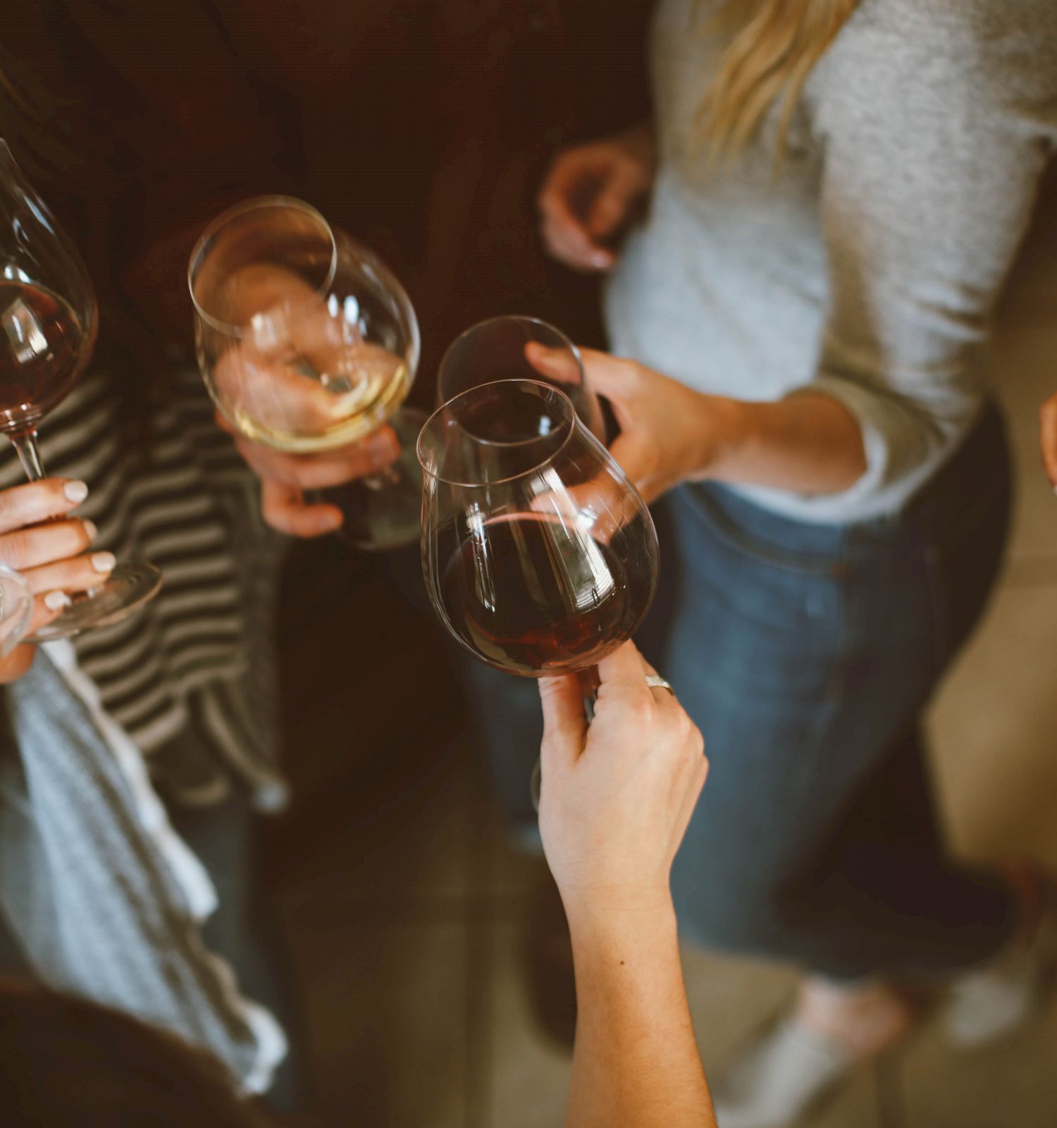 A group of people is gathered, holding and clinking glasses of wine, suggesting a social celebration or toast, seen from a top-down perspective.