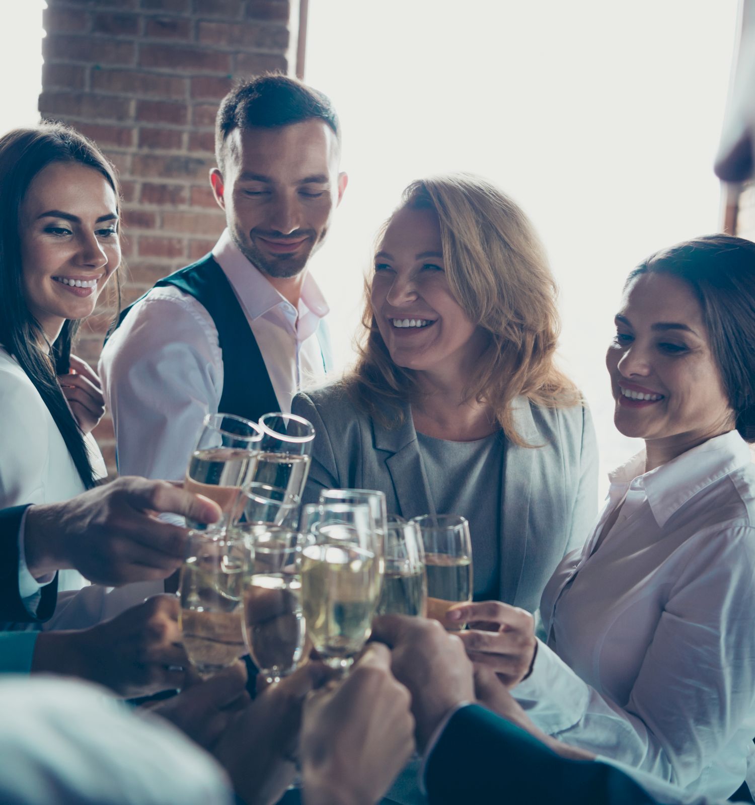 A group of people dressed in business attire are gathered together, smiling and raising glasses for a toast in a celebratory moment.