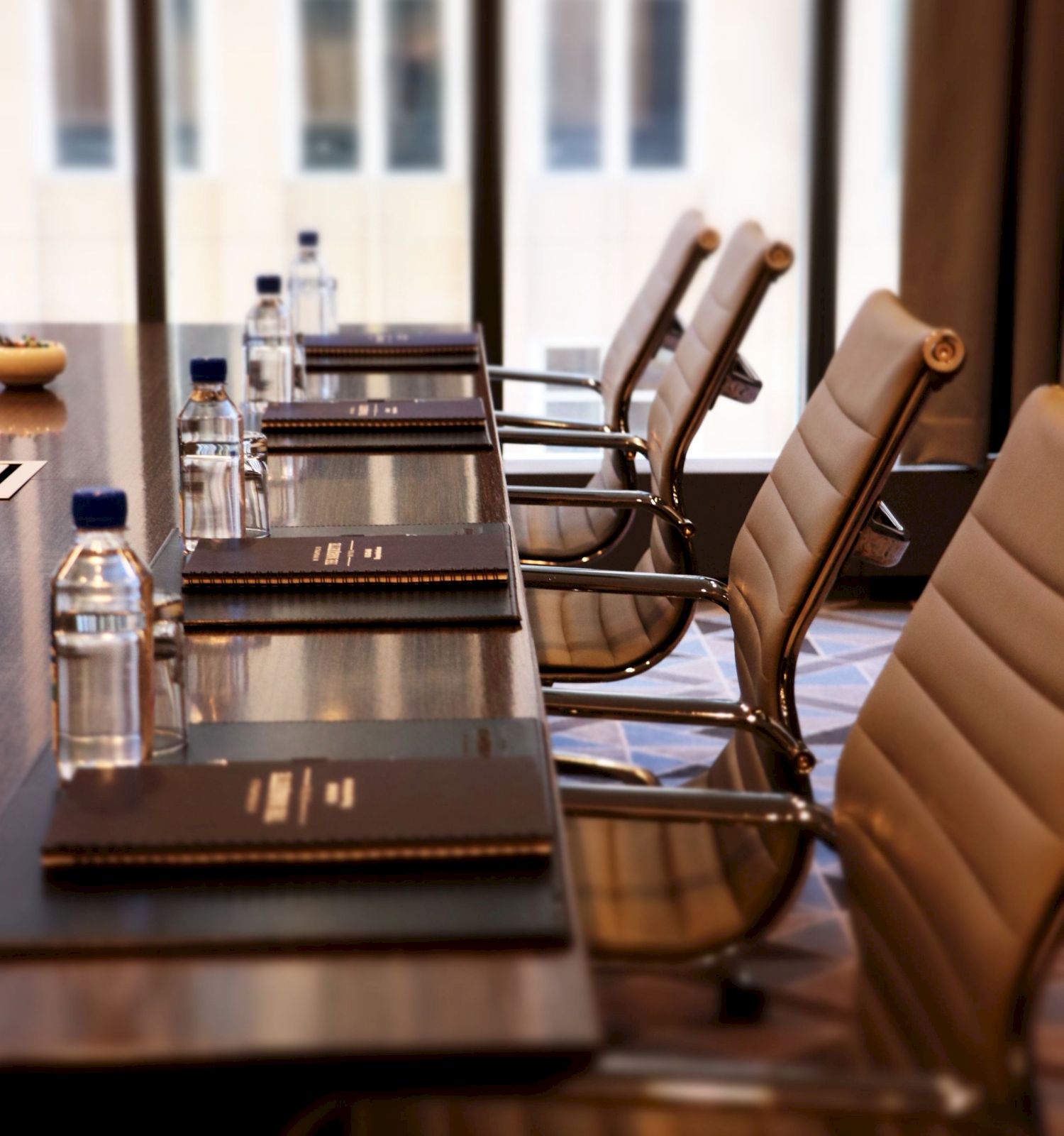 A conference room with a table, executive chairs, notebooks, and water bottles, situated in front of large windows overlooking a building.