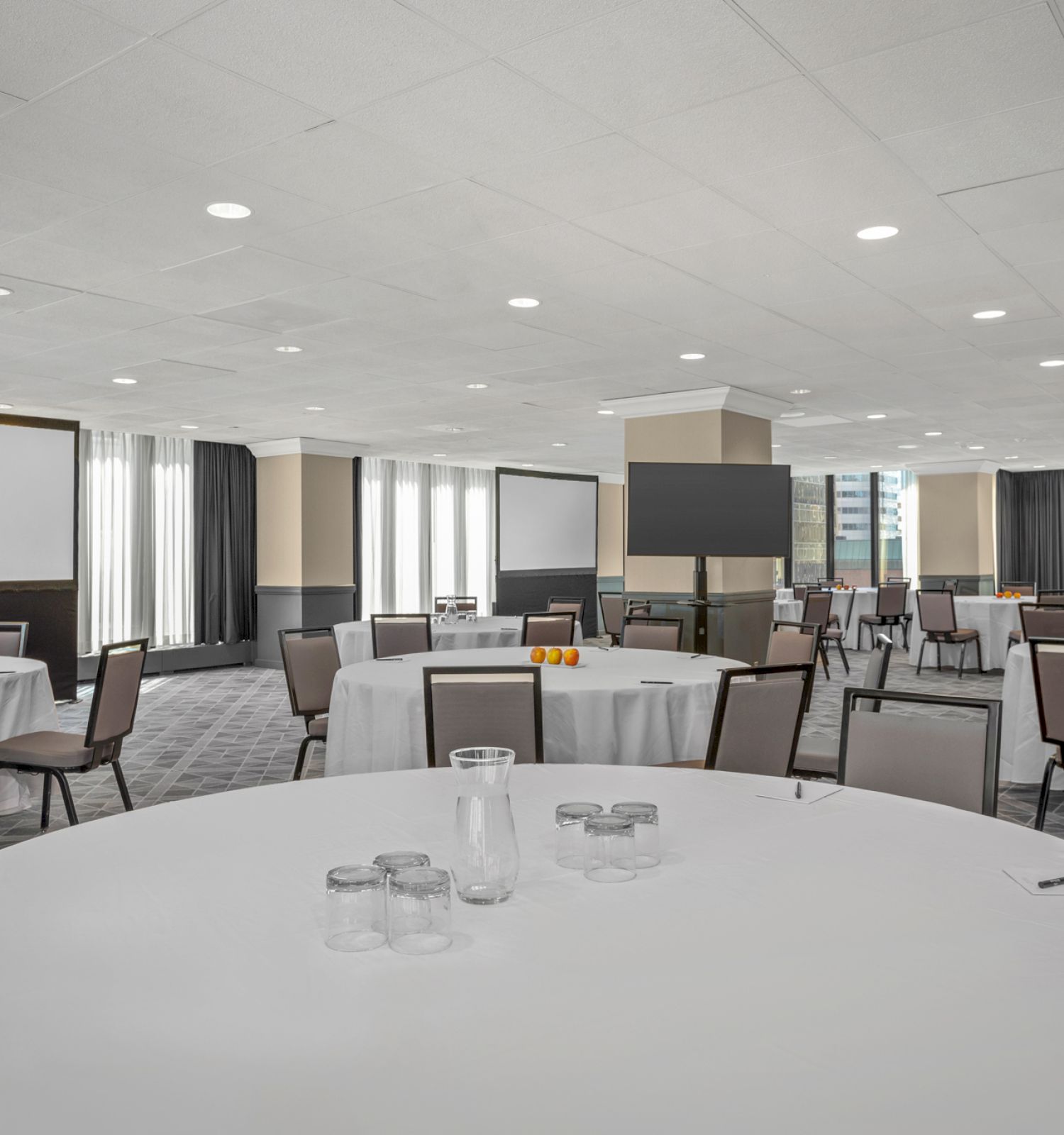 A conference room with round tables and chairs, white tablecloths, water glasses, and presentation screens is pictured.