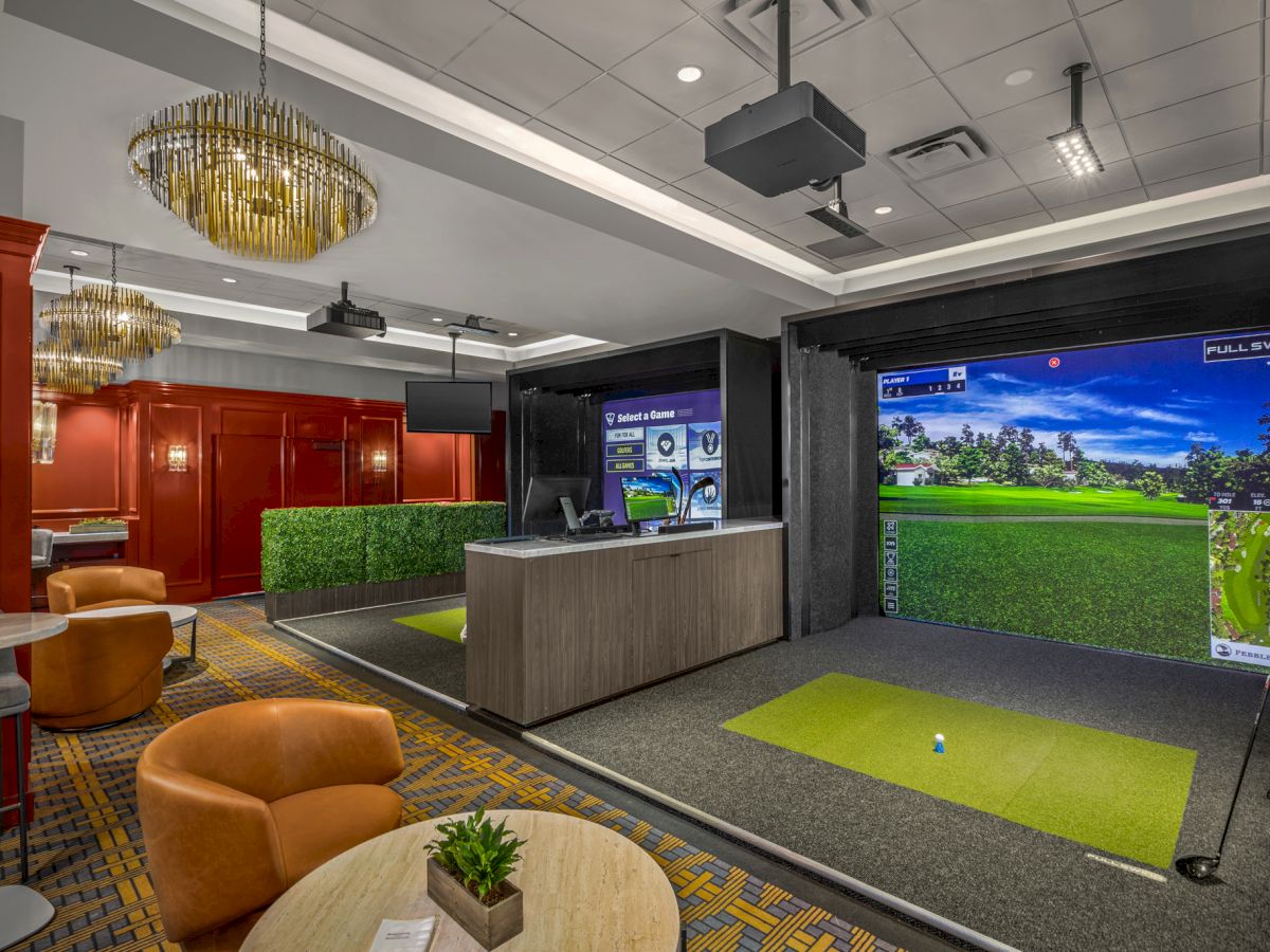 The image shows an indoor golf simulator room with artificial turf, seating area, and modern lighting. A virtual golf course is displayed on screens.