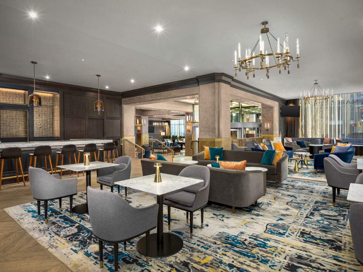 A modern, elegant lounge area with grey and blue furniture, a bar with high stools, and a chandelier, featuring a contemporary design and decor.