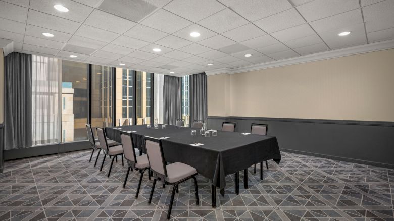 A conference room with a rectangular table covered with a black tablecloth, surrounded by eight chairs, and large windows with city views.