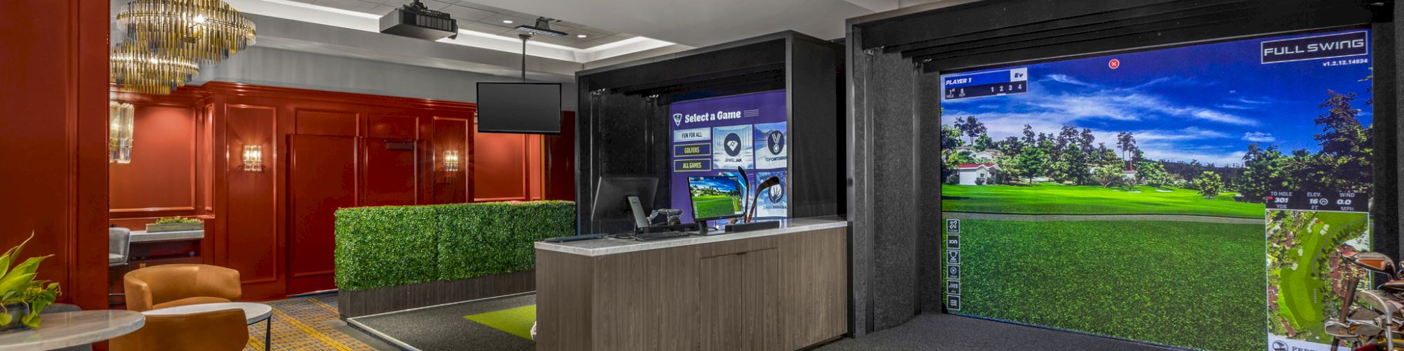 The image shows an indoor golf simulator setup in a stylish room, featuring chairs, a table, and modern lighting fixtures on the ceiling.