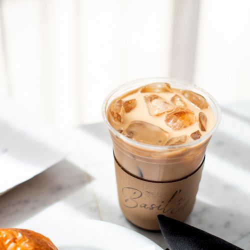 An iced coffee in a plastic cup with a sleeve, next to a bagel and cream cheese on a table.