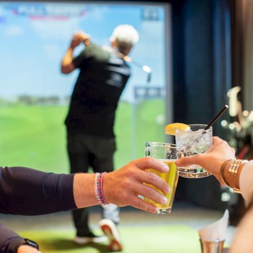 People are toasting drinks while a golfer plays in a virtual golf setup, creating a fun and relaxed atmosphere.