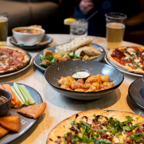 A table filled with pizzas, fries, appetizers, and drinks, providing a delicious spread for a shared meal among friends or family.