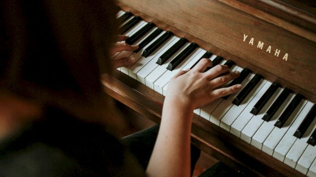 A child plays a wooden Yamaha piano, small hands on the keys, focus on the instrument, warm tones from the wood, intimate music moment.