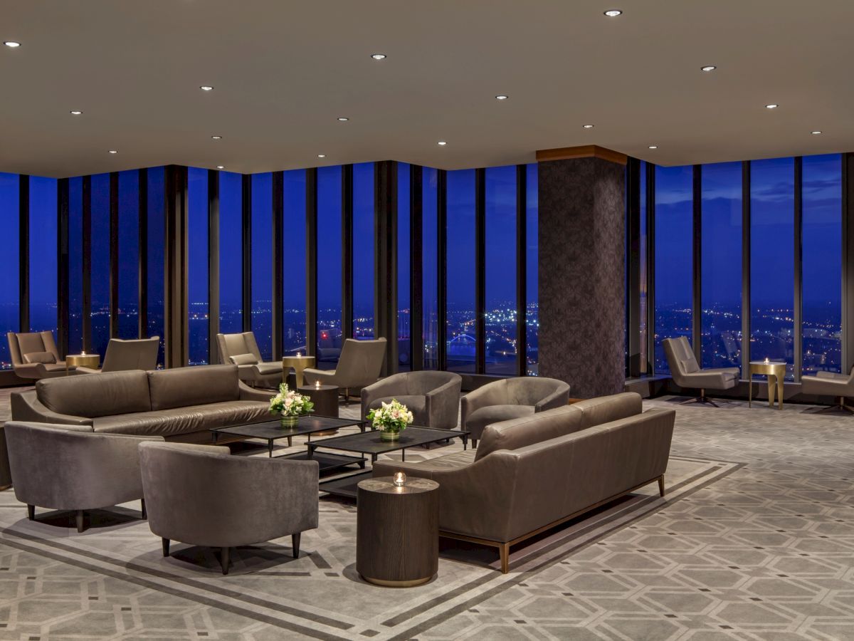 A luxurious hotel lounge with dark sofas, glass coffee tables, and tall windows offering a city-night skyline view, chic and inviting.