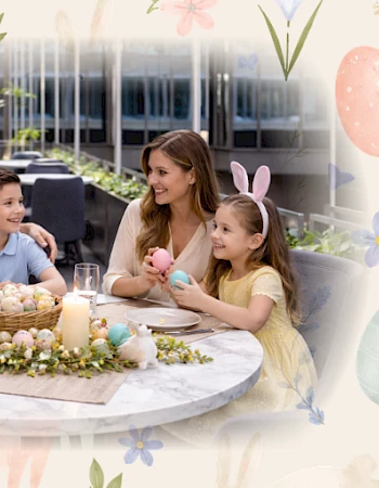 A family of four enjoys Easter treats at a decorated table on a sunny patio. The kids wear bunny ears, and the parents smile warmly.