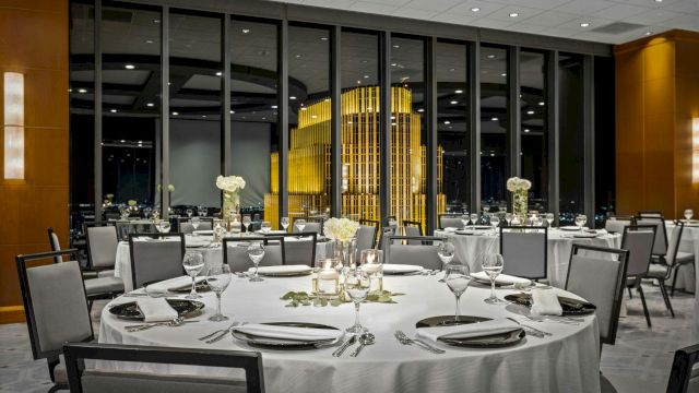 A fancy banquet hall with round tables set for dining, white linens, glassware, silverware, and soft floral centerpieces, preparing for a formal event.