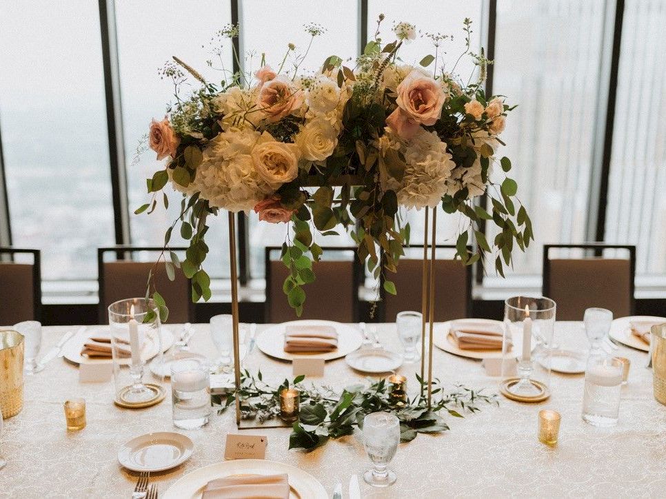 A formal dining table setup with a tall floral centerpiece, candles, plates, and glassware. (140 chars)