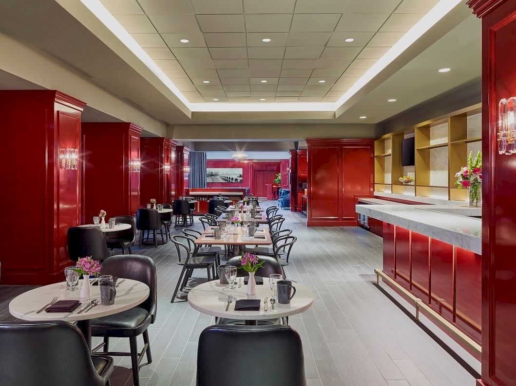 A stylish restaurant or hotel dining area with red glossy partitions, round tables set with plates, and a bar/serving counter to the right, ready for guests.