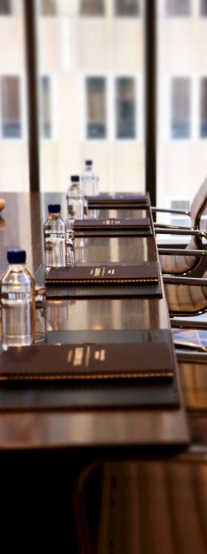 A conference room with a table, chairs, notebooks, and water bottles, located next to large windows with a city view can be seen in the image.