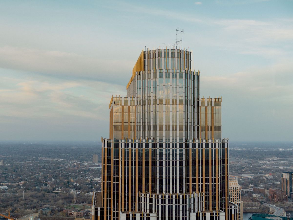 A high-rise building with a tiered architectural design rises above a cityscape under a partly cloudy sky, showcasing modern urban architecture.