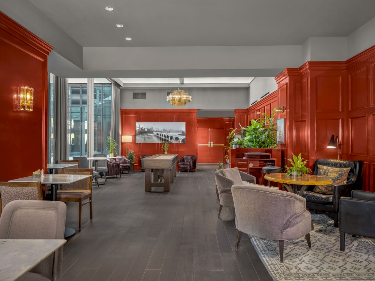 A stylish lounge with red-paneled walls, comfortable seating, a pool table in the center, and a mix of modern and classic decor with ample lighting.