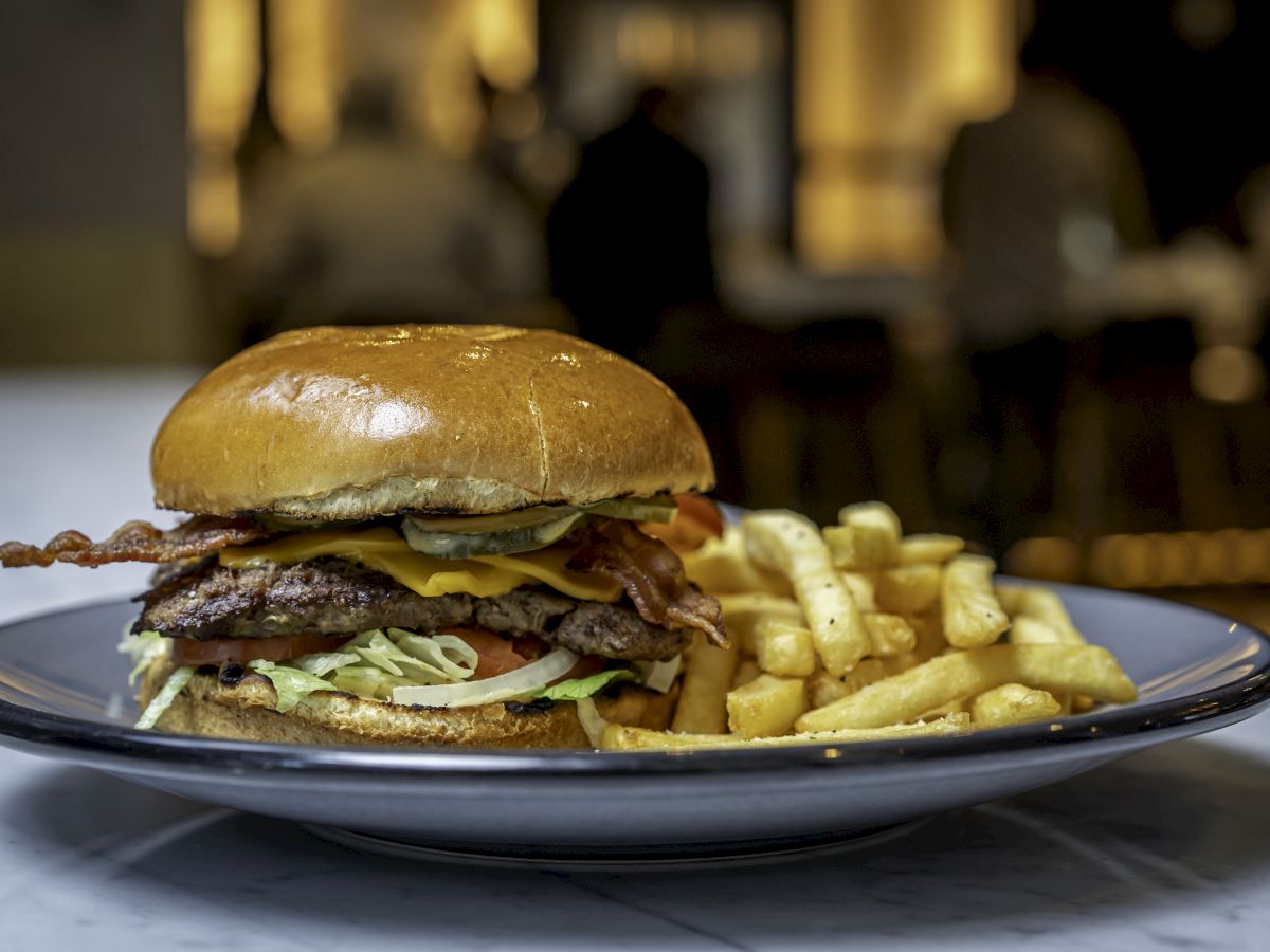 A delicious-looking cheeseburger with bacon, lettuce, and tomato, accompanied by a side of golden French fries on a plate.