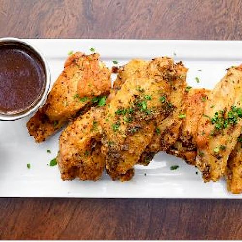 The image shows a rectangular plate with seasoned chicken wings, garnished with herbs, and two dipping sauces on the side.