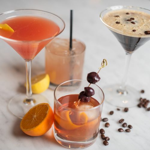 The image shows four cocktails with garnishes, coffee beans, and an orange slice on a marble surface.