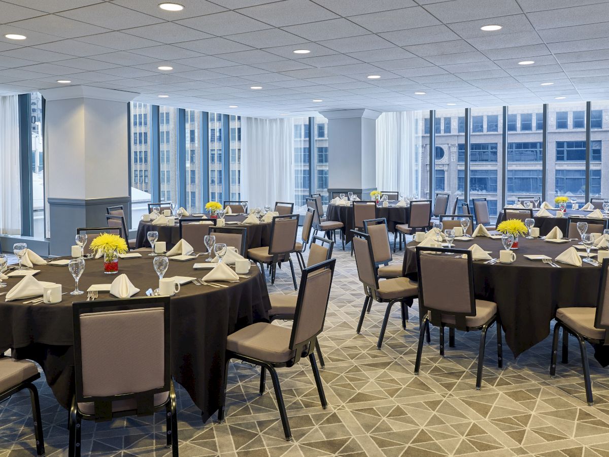 A well-lit banquet room set up for an event with round tables, chairs, window views, and floral centerpieces.