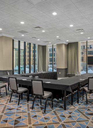 A conference room with a U-shaped table setup, modern decor, ample seating, large windows, a TV screen, and geometric-patterned carpet ending the sentence.