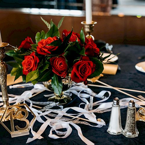 A beautifully decorated table with red roses, gold candle holders, salt and pepper shakers, and a table number 13, adorned with ribbons.