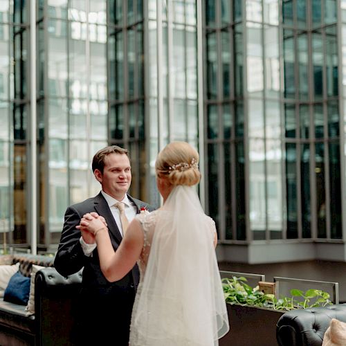 A bride and groom hold hands in an outdoor setting surrounded by modern glass buildings, captured in a seemingly tender moment.