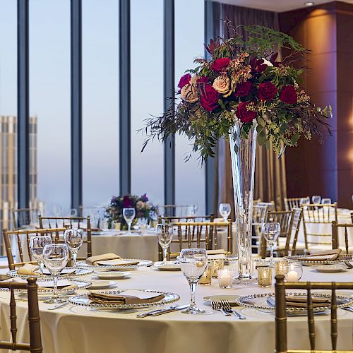 Elegant table setting for an event in a high-rise building, with floral centerpieces, fine china, and cityscape views through large windows.