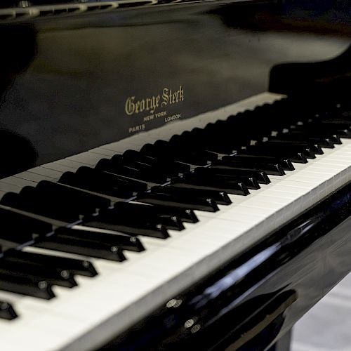 A close-up image of a black grand piano with visible white and black keys. The piano brand 