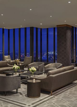 A modern lounge with elegant furniture, large windows offering a nighttime city view, soft lighting, and a sophisticated atmosphere.