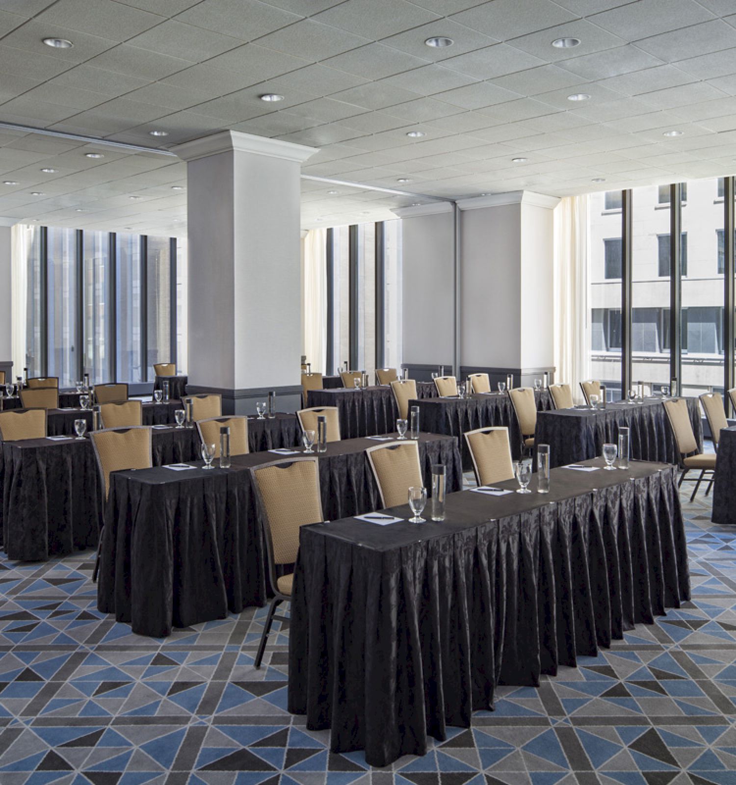 The image shows a large, well-lit conference room with multiple rectangular tables and chairs arranged in rows, ready for a meeting or seminar.