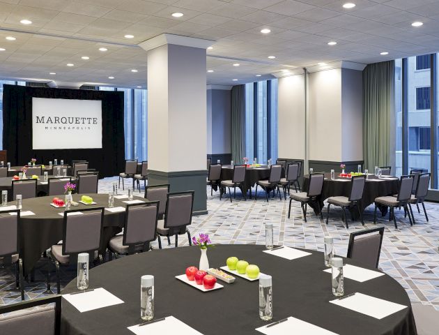 This image shows a conference room setup with round tables, chairs, water bottles, notepads, and a projector screen displaying "Marquette."