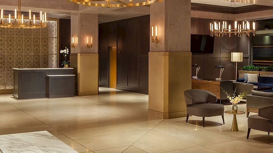 A spacious, modern lobby with elegant chandeliers, seating areas, a reception desk, and sophisticated decor including plants and flowers.