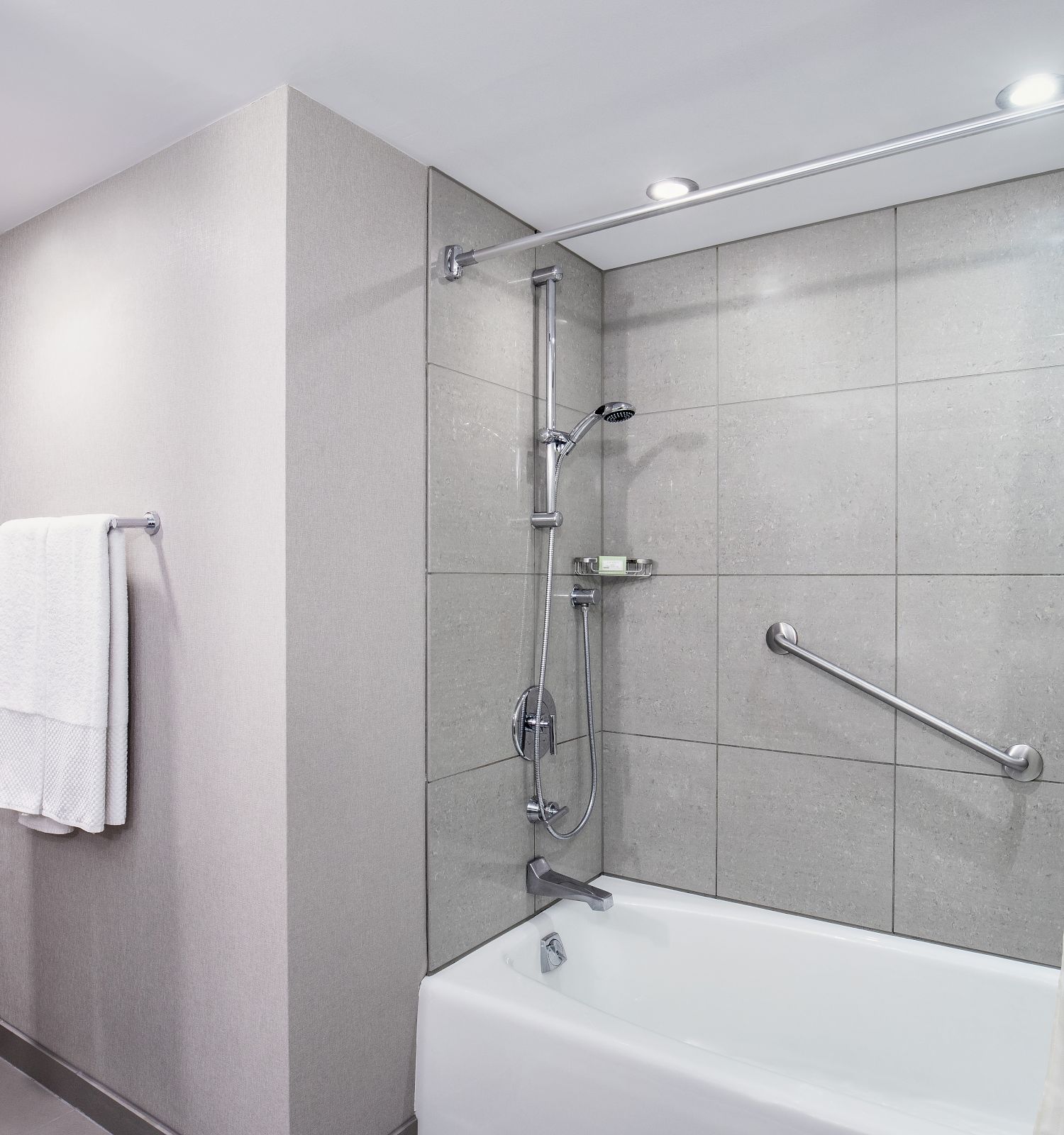 A bathroom with a modern design, featuring a bathtub, shower, grab bar, towel rack, and wall art, illuminated by overhead lighting.