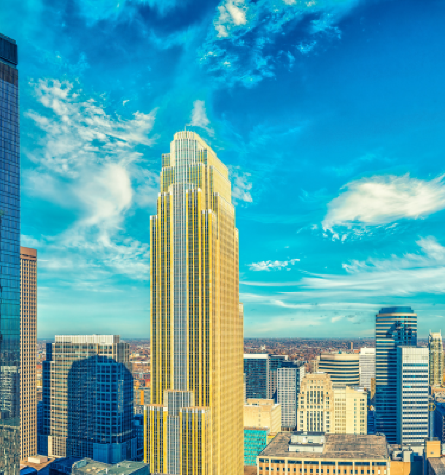 A city skyline featuring tall skyscrapers under a bright blue sky with scattered clouds.